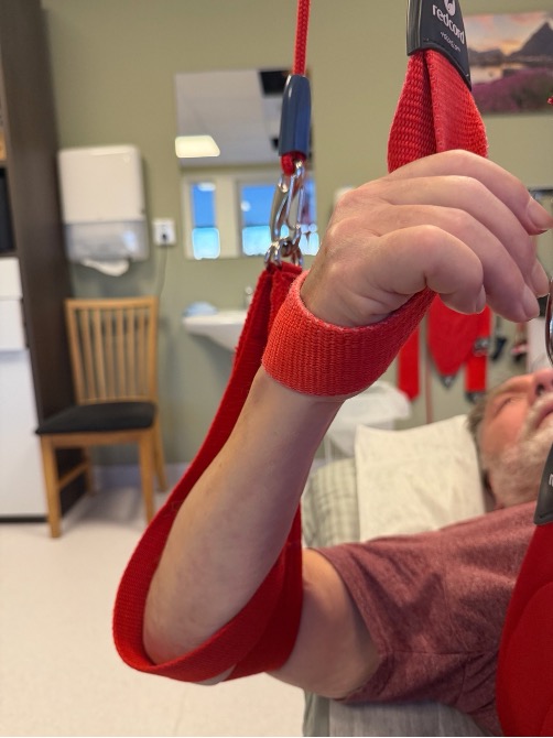 A man's arm and hand supported in red Redcord slings during a stroke rehabilitation session